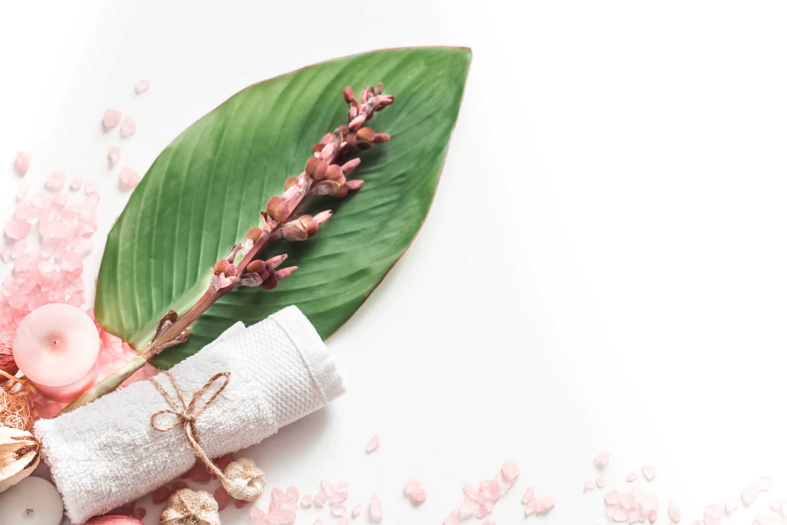 imagem de fundo branco com uma folha, toalha e velas, além de pedrinhas de sal rosa dando a ideia de cuidados com o corpo