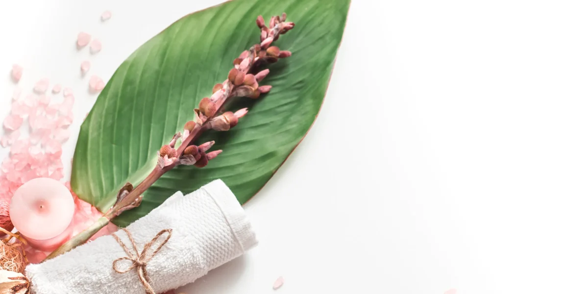 imagem de fundo branco com uma folha, toalha e velas, além de pedrinhas de sal rosa dando a ideia de cuidados com o corpo